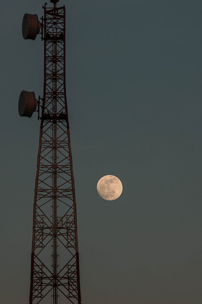 Telecom tower silhouetted against a full moon at twilight, creating an industrial yet serene scene.